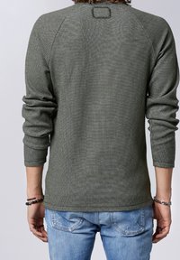 Pull texturé vert olive avec un col rond et des manches longues, présentant un subtil détail cousu à l'arrière et des poignets ajustés.