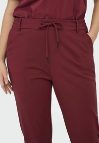 Pehmeästä materiaalista valmistetut viininpunaiset jogger-housut, joissa kiristysnyöri vyötäröllä ja sivutaskut. Tyylikäs muotoilu ja sileä pinta.