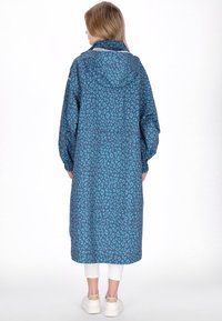 Pitkä sininen hupullinen sadetakki, jossa tummansininen leopardikuviointi. Varustettu joustavilla resoreilla hihoissa ja rento istuvuus.