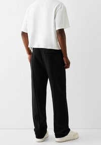 Svarta sweatpants med sid sömmar och en bakficka, är kombinerat med en vit kort topp. Skorna är ljusa med en texturerad sula.