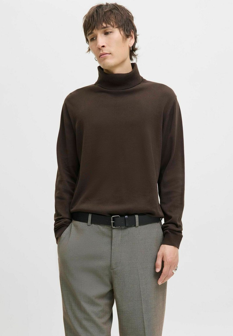 Brown turtleneck sweater in soft fabric, paired with grey trousers. The outfit features a black belt with a silver buckle.