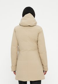 Beige gewatteerde jas met capuchon, voorzien van een gladde textuur en een getailleerd silhouet, dat tot halverwege de bovenbenen reikt. Geen zichtbare branding of hardware.