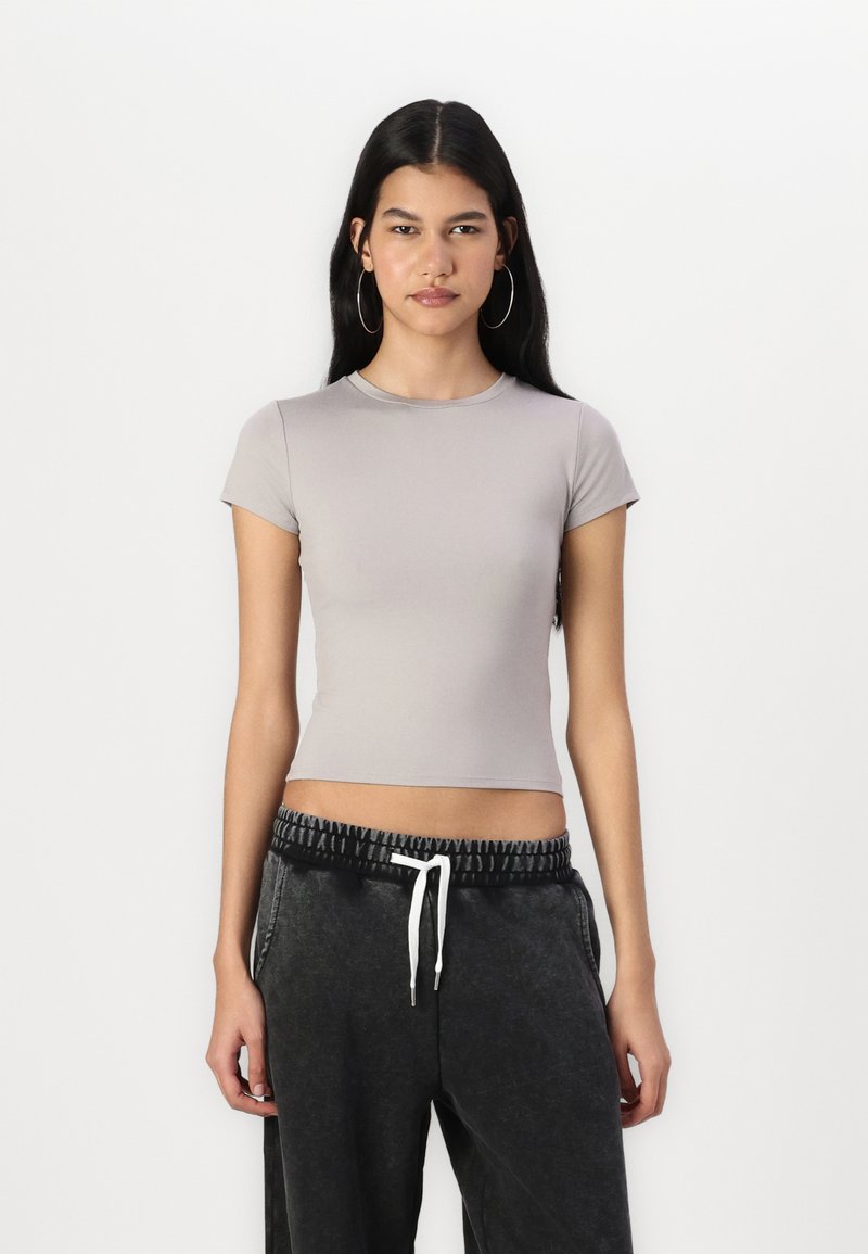 Tricou scurt, gri, ajustat, cu mâneci scurte, decolteu rotund, și textură netedă. Asortat cu pantaloni negri cu șnur, având o talie texturată.
