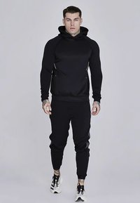 Sudadera deportiva negra con diseño ajustado, con capucha forrada y bolsillos laterales; combinada con pantalones a juego y zapatillas.