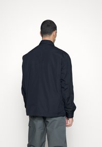 Navy lightweight jacket with a collar, buttoned cuffs, and a slightly loose fit. Smooth texture with no visible patterns or accents.
