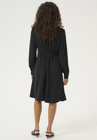 Robe noire à manches longues avec une taille élastique, longueur mi-mollet, tissu lisse, poignets boutonnés et coupe décontractée. Design simple et classique.