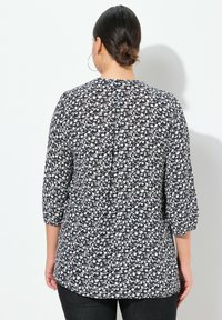 Blusa a stampa floreale in bianco e nero con maniche tre quarti, scollatura rotonda e un leggero dettaglio a piega sul retro. Tessuto morbido.