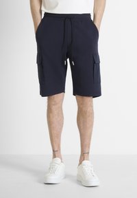 Pantalones cortos de carga en color marino hechos de una tela suave, con dos bolsillos laterales y una cintura con cordón ajustable, combinados con zapatillas blancas.