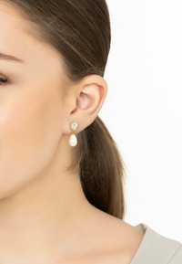 Los pendientes de gota de oro presentan un acento de cristal transparente con una perla en forma de lágrima debajo. Acabado suave con un brillo pulido. Diseño elegante.