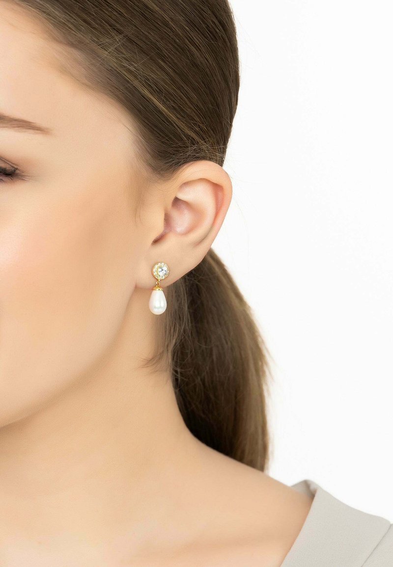 Los pendientes de gota de oro presentan un acento de cristal transparente con una perla en forma de lágrima debajo. Acabado suave con un brillo pulido. Diseño elegante.