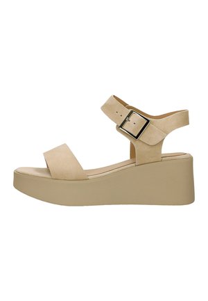 Beige sleehaksandaal met een dikke zool, open teen, enkelbandje en grote vierkante metalen gesp voor aanpassing.