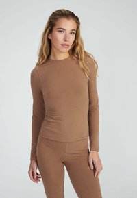 Top a maniche lunghe, aderente, in tessuto marrone opaco. Texture liscia, design a collo tondo, abbinato a pantaloni aderenti dello stesso colore.