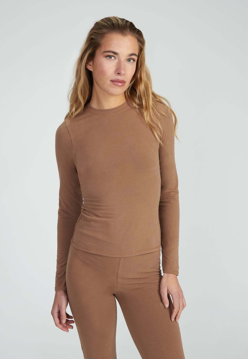 Top a maniche lunghe, aderente, in tessuto marrone opaco. Texture liscia, design a collo tondo, abbinato a pantaloni aderenti dello stesso colore.