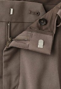 Pantalones marrones con cremallera, botón y broche de metal. La tela tiene un tejido texturizado y un acabado duradero.