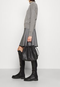 Czarna skórzana torba typu bucket z zebranym u góry, szara bluza, spódnica w wzór houndstooth oraz czarne kozaki sięgające do kolan. Skup się na fakturach i wzorach.
