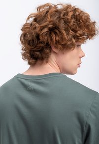 Grijs-groene katoenen t-shirt met een klassieke ronde hals; heeft een subtiele logodetail op de achterkant nabij de halslijn; zachte textuur.