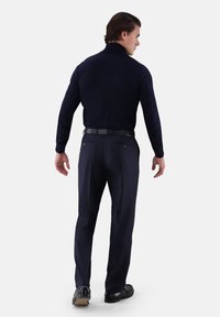 Marineblauer Pullover mit hohem Kragen, kombiniert mit dunkler Hose. Verfügt über ein tailliertes Design und eine glatte Textur, ergänzt durch einen schwarzen Gürtel und Schuhe.