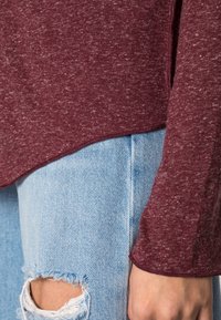 Mörkröd långärmad topp med en texturerad väv, parat med ljusblå slitna jeans med fransade kanter och en liten reva.