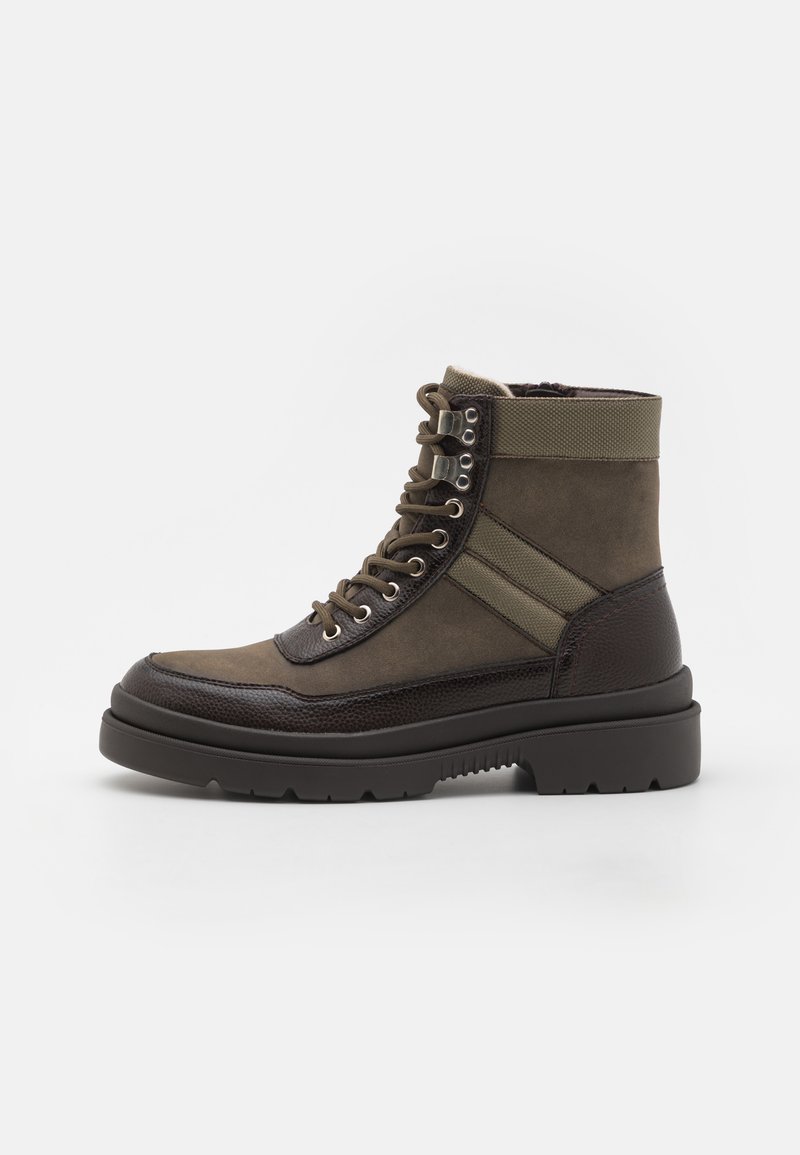 Green and brown ankle boot with a textured upper, metal eyelets, lace-up front, and a thick black rubber sole. Features contrasting stripes.