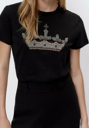 Sort t-shirt med krone-design dekoreret med sølv- og røde detaljer. Korte ærmer og rund halsudskæring.