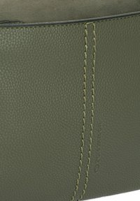 Cuero verde texturizado con costuras visibles y un logo sutil. Presenta una superficie suave y una forma cilíndrica.