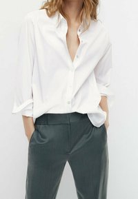 Witte button-up shirt met opgerolde mouwen, gecombineerd met grijze broek met een gestructureerde tailleband en een relaxed fit.