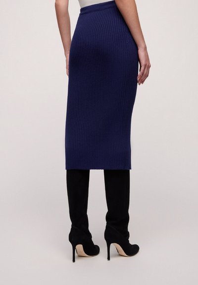 Knit pencil skirt in dark blue with a ribbed texture, featuring a fitted design that reaches mid-calf, paired with black stiletto boots.
