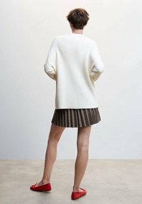 Pull blanc surdimensionné en maille côtelée, jupe plissée marron et ballerines rouges. Maille texturée, coupe décontractée et design superposé mettant l'accent sur des couleurs neutres et vives.