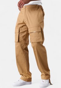 Cargo pants in tan cotton fabric, featuring side pockets, elasticized waist, straight leg design, and subtle branding detail.