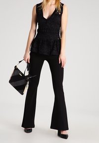 Czarny top peplum z teksturowanym kwiecistym wzorem, w połączeniu z czarnymi spodniami z rozszerzanymi nogawkami i paskowaną torebką. Całość dopełniają czarne buty na obcasie z zakrytymi palcami.
