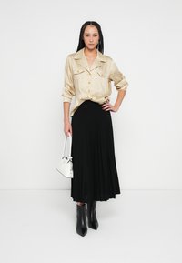 Zlatá vzorovaná košeľa na gombíky so zrolovanými rukávmi, čierna plisovaná sukňa a čierne členkové topánky. Bielu kabelku dopĺňa tento outfit.