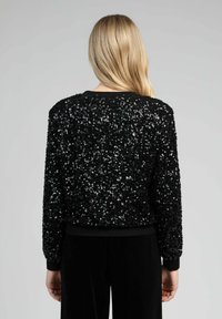 Sweatshirt en sequins noirs avec un col rond, des poignets et un ourlet côtelés. Présente une surface texturée et brillante due aux sequins superposés.