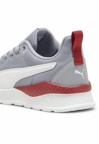 Šedá sportovní bota s vrchní částí z prodyšné tkaniny, bílými akcenty, červenou patou a texturovanou mezipodešví. Má zaoblený tvar a design na šněrování.