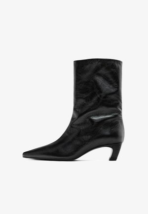 Černý kožený kotníkový bot s špičatou špičkou a středním podpatkem. Hladký povrch s jemnými vráskami, s elegantním siluetou a minimalistickým designem.