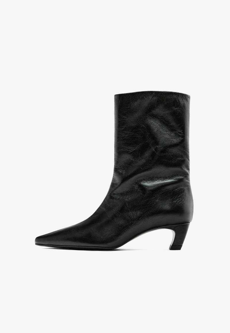 Černý kožený kotníkový bot s špičatou špičkou a středním podpatkem. Hladký povrch s jemnými vráskami, s elegantním siluetou a minimalistickým designem.