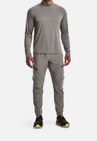 Graues, langärmliges Sportoberteil, kombiniert mit passenden, schmal zulaufenden Hosen, die über Reißverschlusstaschen verfügen und aus einem glatten, dehnbaren Stoff gefertigt sind.