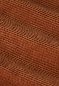 Tissu en velours côtelé marron avec une texture nervurée, présentant des lignes horizontales et une apparence douce et moelleuse. Couleur uniforme sur toute la surface.