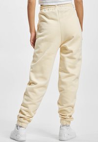 Pantaloni de trening de culoare crem cu un talie elastică, glezne cu manșete și o textură moale. purtați cu adidași albi.
