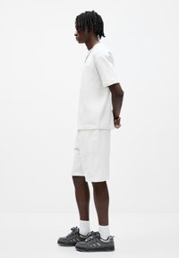 Ensemble en t-shirt en coton blanc et short, avec une coupe décontractée. Paire de baskets noires avec des accents contrastants et des chaussettes blanches.