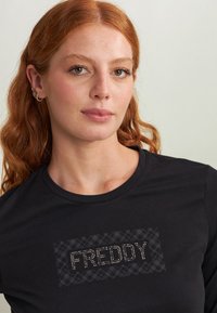 T-shirt nera con un design testurizzato e la scritta "FREDDY" in strass. Maniche corte e scollatura rotonda. Tessuto dalla superficie liscia.