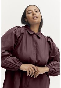 Maroon button-up shirt with puffed sleeves and a collar. The fabric appears smooth, featuring elasticized cuffs and a relaxed fit.