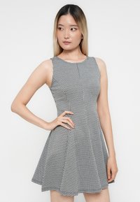 Svartvit houndstooth-mönstrad klänning med ärmlös design, rund halsringning, figurnära överdel och utsvängd kjol. Slät tygstruktur.