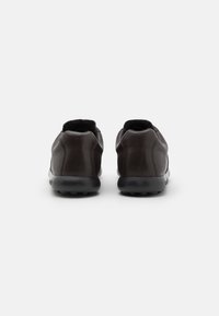 Scarpe in pelle marrone scuro con profilo basso, forma arrotondata e suole in gomma. Design semplice, caratterizzato da una texture liscia e accenti minimi.