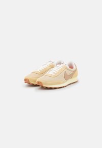 Beige athletic shoes with a mesh upper, suede accents, and white laces. Features a brown swoosh logo and a textured rubber outsole.