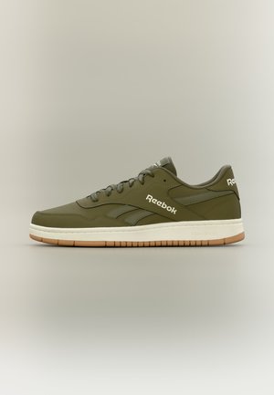 Ελιά πράσινο παπούτσι Reebok με λευκή σόλα και γαλακτώδη εξωτερική σόλα, πλευρική όψη σε απλό ανοιχτό φόντο με εμφανές λογότυπο στο πλαϊνό μέρος και τη φτέρνα.