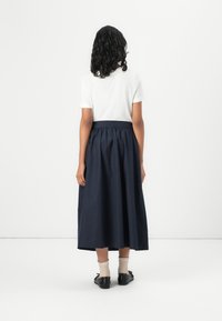 Marine, midje-lang skjørt med rynket midje og flytende design, kombinert med en hvit t-skjorte med korte ermer og svarte snøresko.