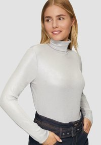 Helles graues Langarmrollkragenoberteil in gerippter Textur mit einem subtilen Glanz, kombiniert mit hoch taillierten, dunklen Jeans.