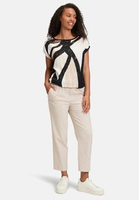 White short-sleeve top with black and beige abstract patterns, paired with light beige cropped pants and white sneakers.
