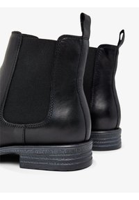 Schwarze Lederstiefeletten mit elastischen Seiteneinsätzen, runden Zehen und gestapelten Absätzen, die eine strukturierte Oberfläche und kontrastierende Nähte aufweisen.