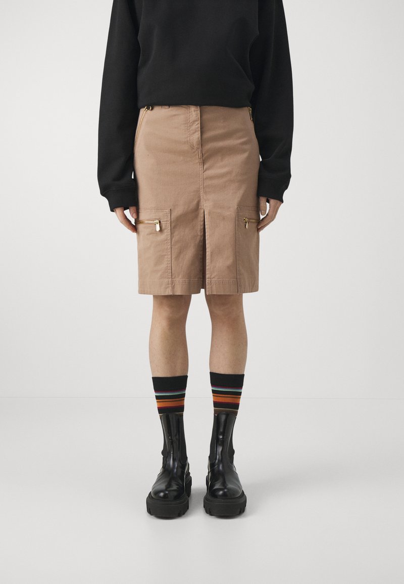 Beige cargo skørt med forkant slids og dobbelte lynlåslommer. Bæret med sorte kampstøvler og flerfarvede stribede sokker, udstyret med en sort sweatshirt.